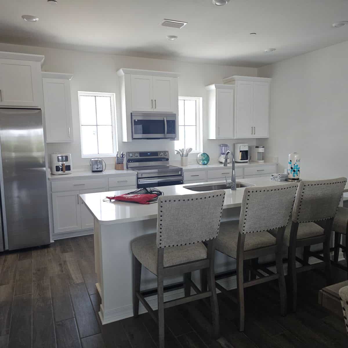 Kitchen with white cabinets, tall stools against the counter, and stainless steel appliance