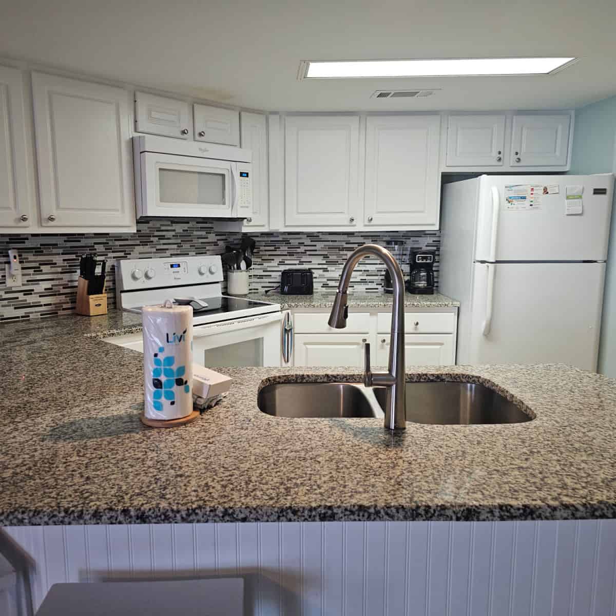 Kitchen with white cabinets and appliances, brown granite countertop