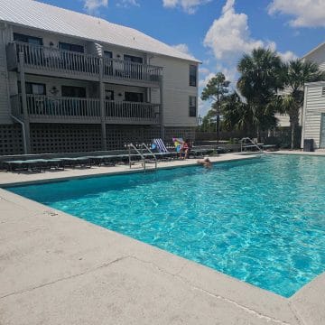 Outdoor pool with lounge chairs around the deck, Two story Cotton Bayou Condo building to the left of the pool