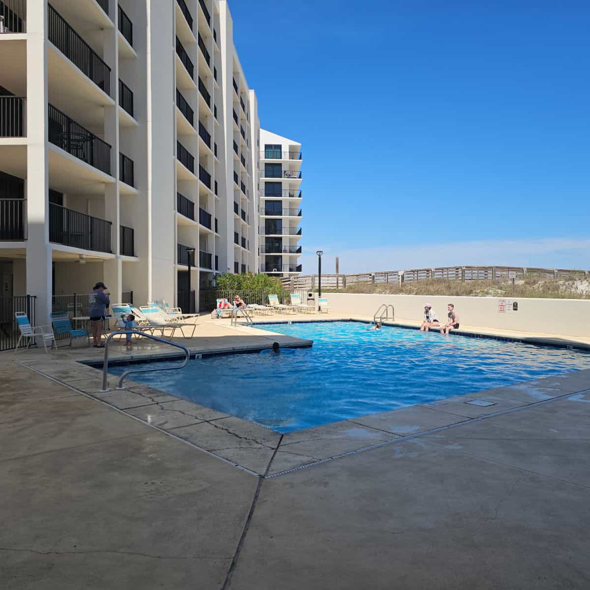 outdoor pool with people sitting on the pool deck next to the Wind Drift building.