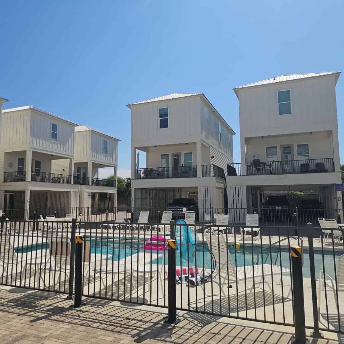 Pelican Place Cottages white buildings around the outdoor pool that has a fence around it and deck chairs