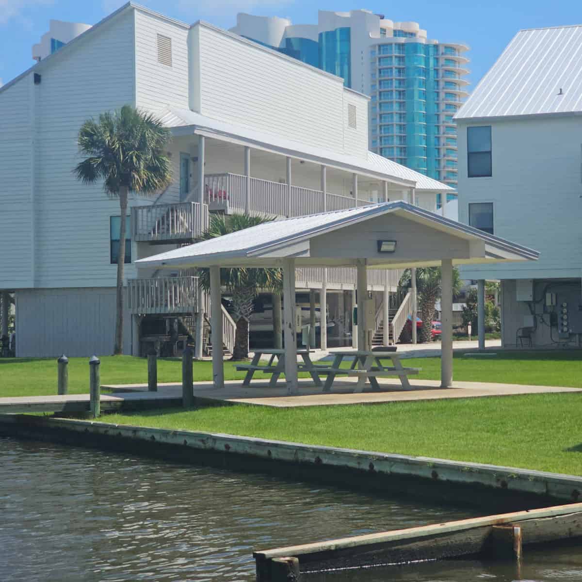 covered picnic area with two picnic tables under it, white Cotton Bayou Condo buildings behind it.