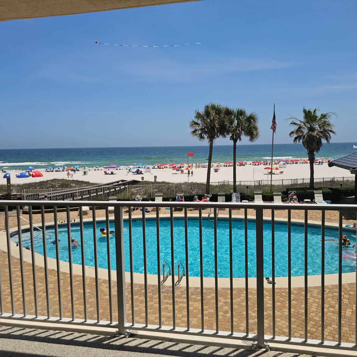 Looking over a balcony to the pool, palm trees, white sand beach and the Gulf with a kite flying on the blue sky