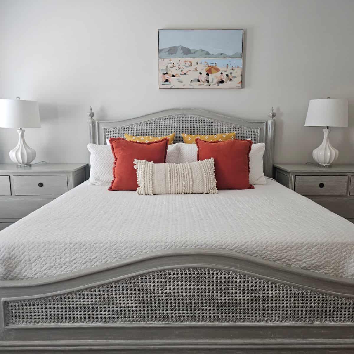 bedroom with lots of pillows on the bed, white lamps on the nightstand, coastal art on the wall