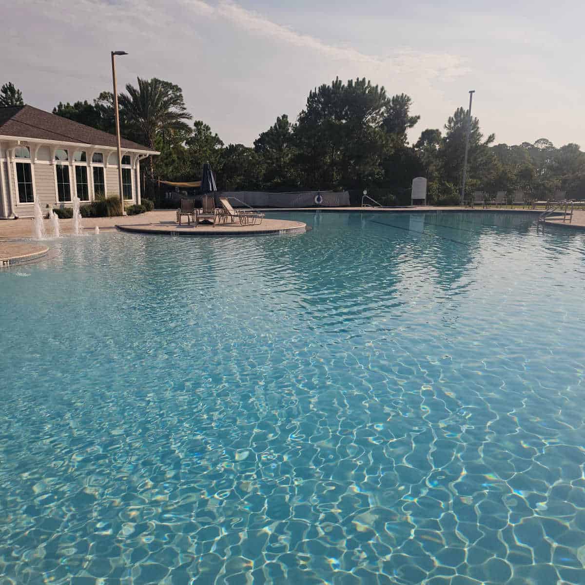 Large outdoor pool with seating around the deck and a building to the left