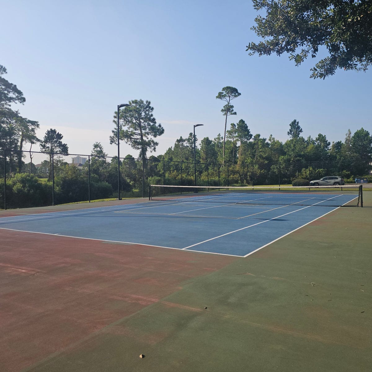 Tennis court with a tall fence around it surrounded by tall trees