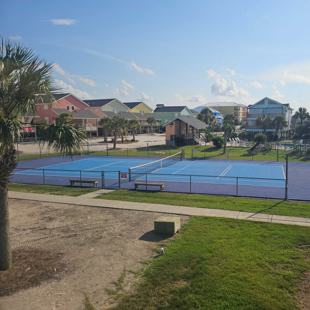 looking out to a tennis court surrounded by colorful houses and a pool in the corner