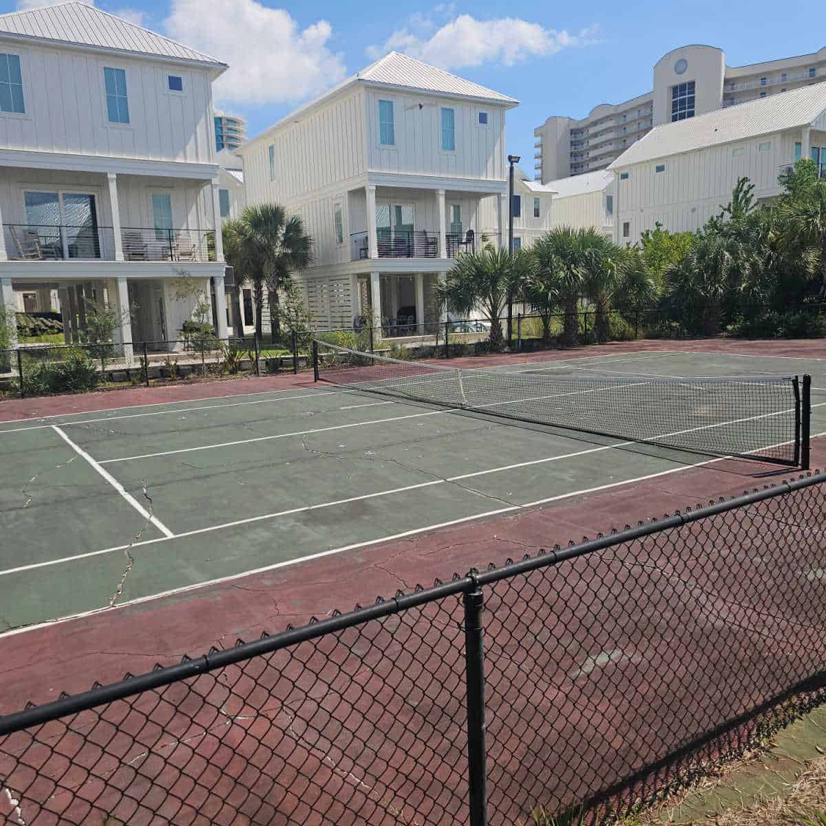 Tennis court with fence around the court, white cottages behind the tennis court
