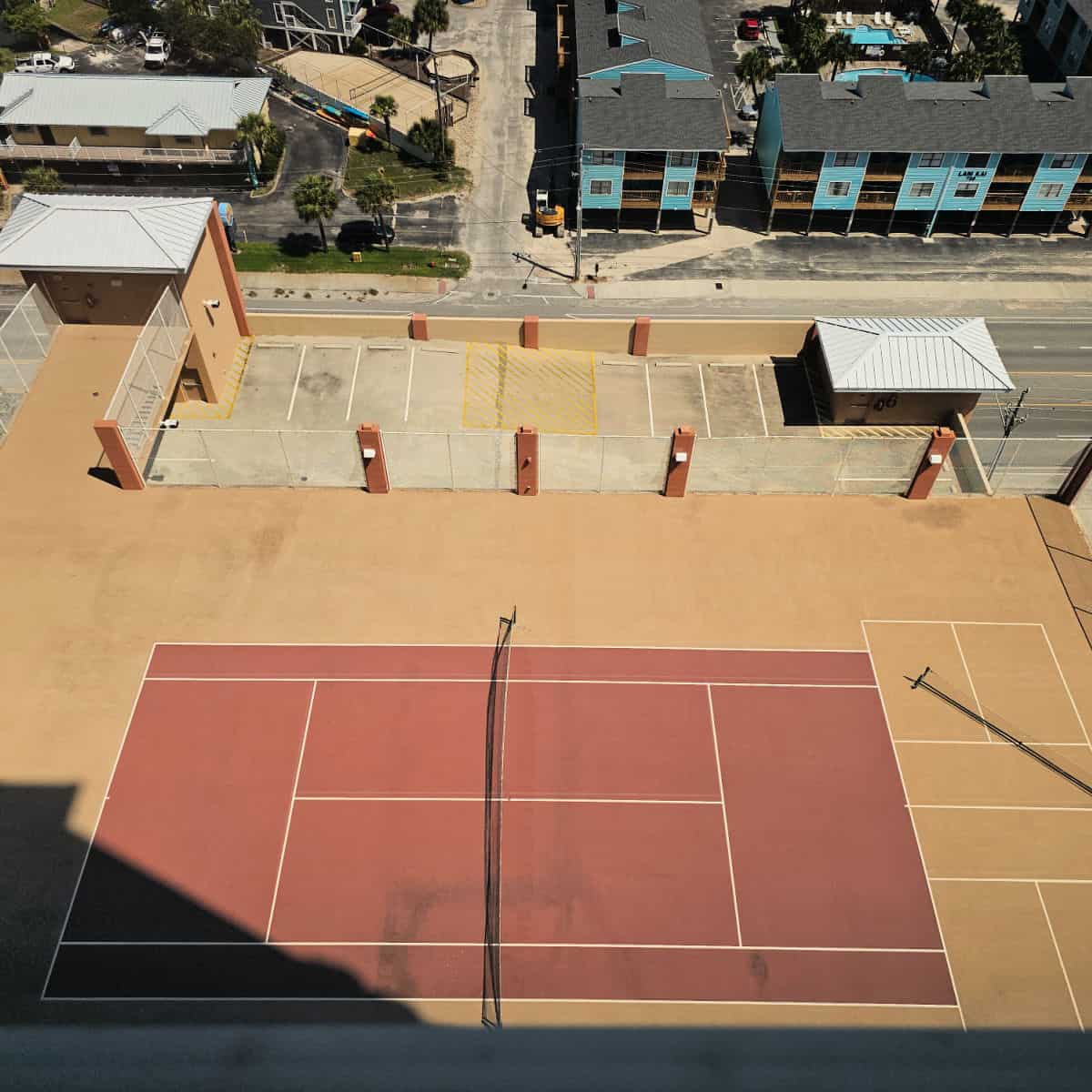 looking down over an outdoor tennis court on top of the Phoenix Gulf Shores parking garage. Blue and brown buildings across the road