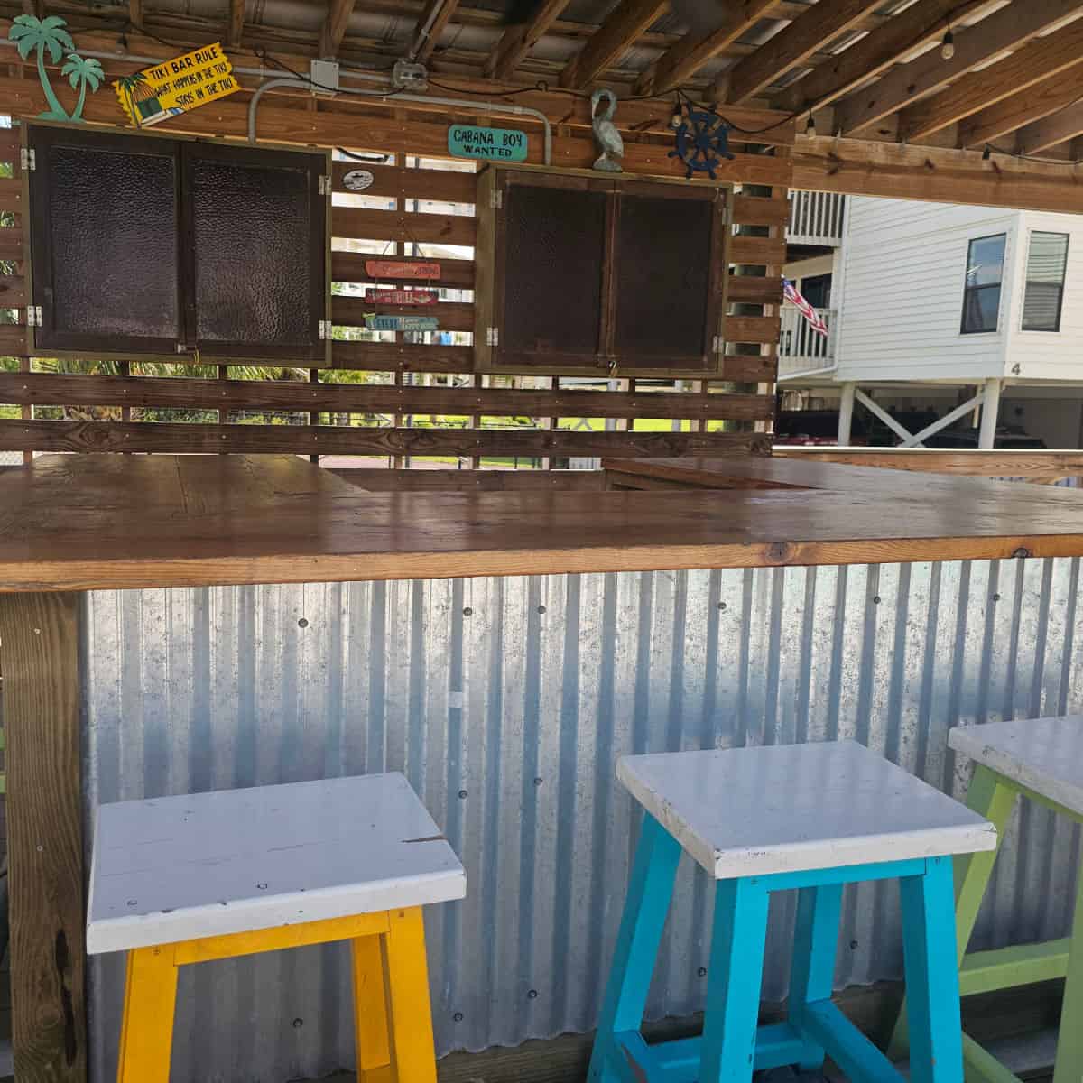 tiki bar with cabinets and wooden counter, colorful stools against the counter