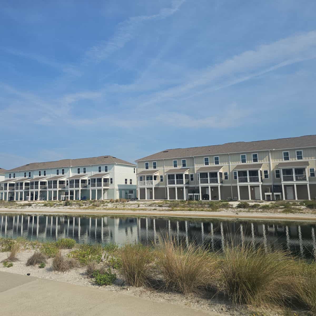 Vacation rental townhome buildings near a large pond with grasses and bushes around the edge