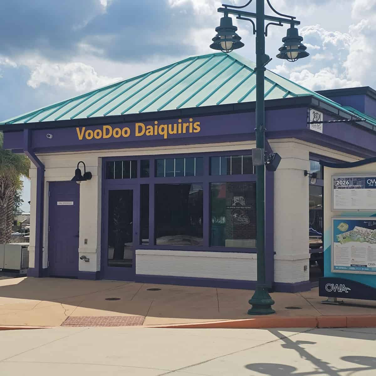 VooDoo Daiquiris name on the side of a purple awning above the entrance to a building. OWA events sign on the right