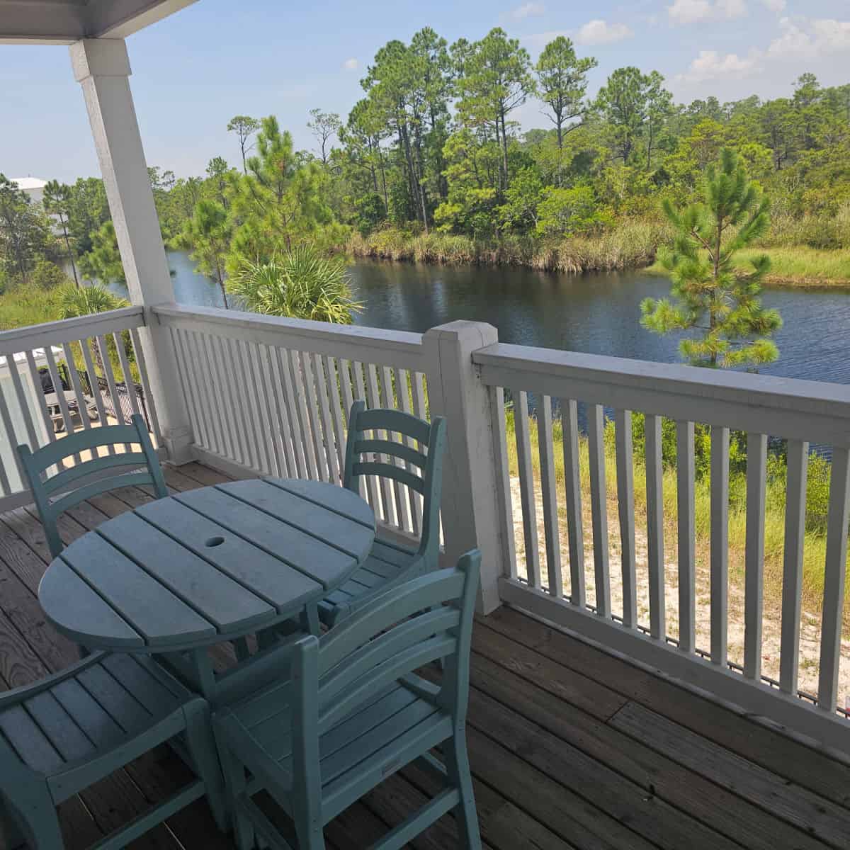 deck with blue table and chairs looking over water with tall trees along side the bank