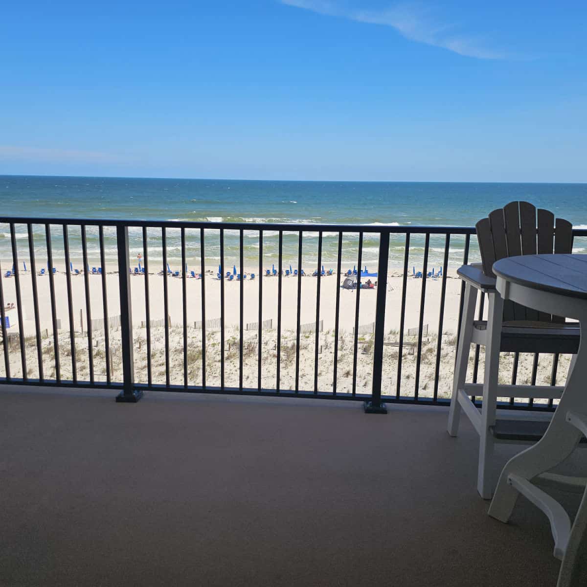 Looking over the balcony to the Gulf with white sandy beach, portion of a table and chairs on the right side