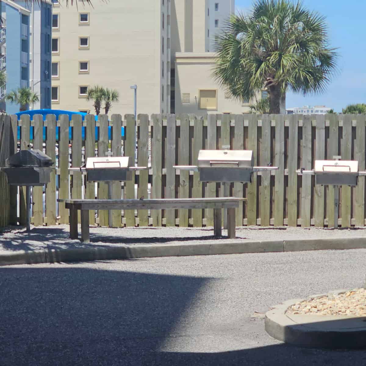 charcoal grills by a fence with a wooden bench neear them