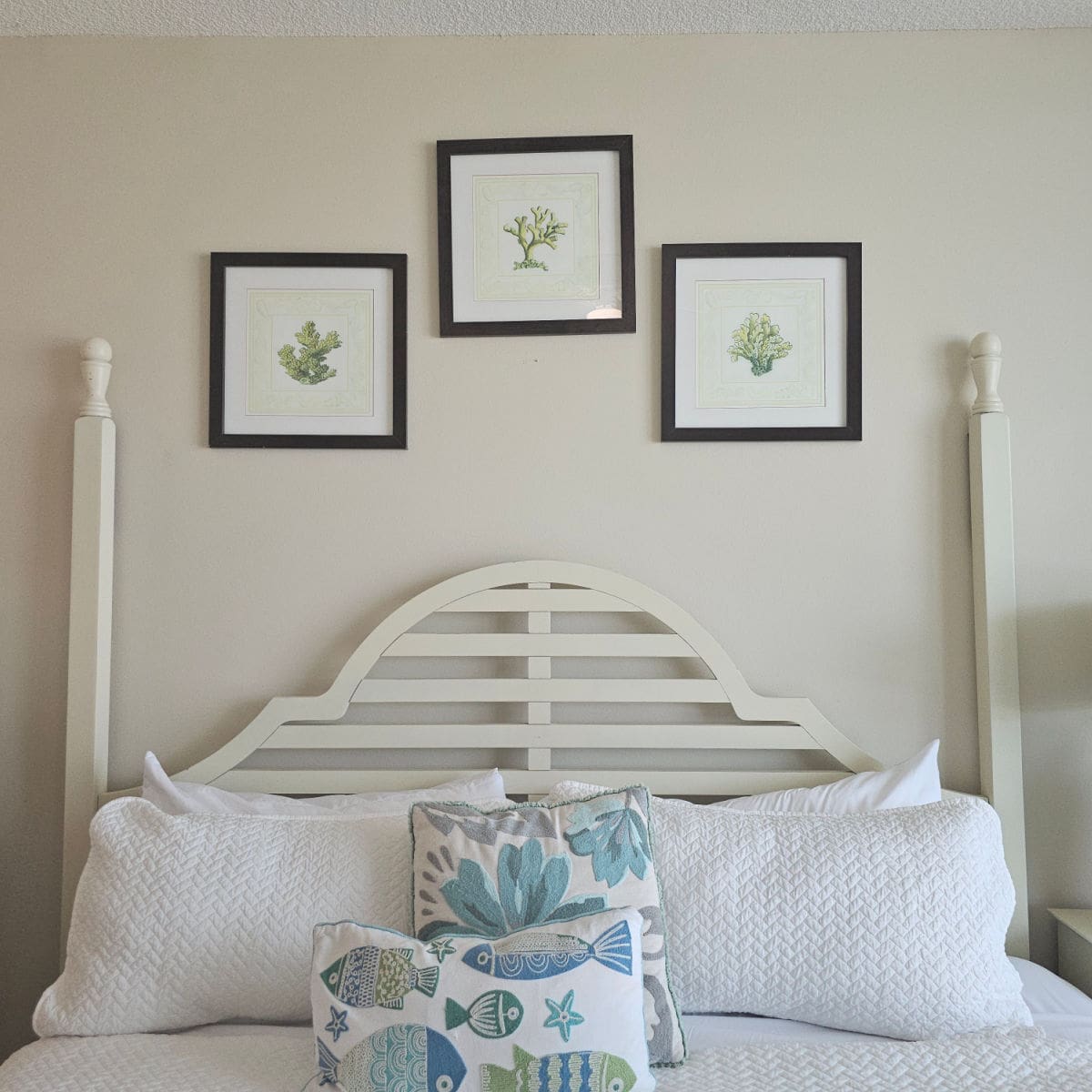 Bedroom with white linens, fish and leaf pillows, coral art on the wall