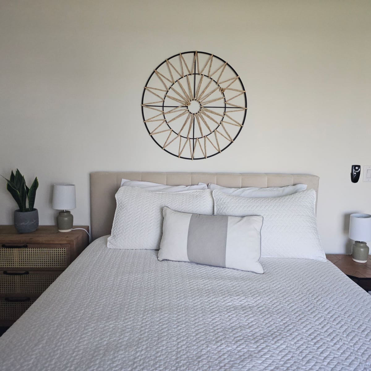 bedroom with circle yard art above the white linen covered bed, nightstands with lamps on either side