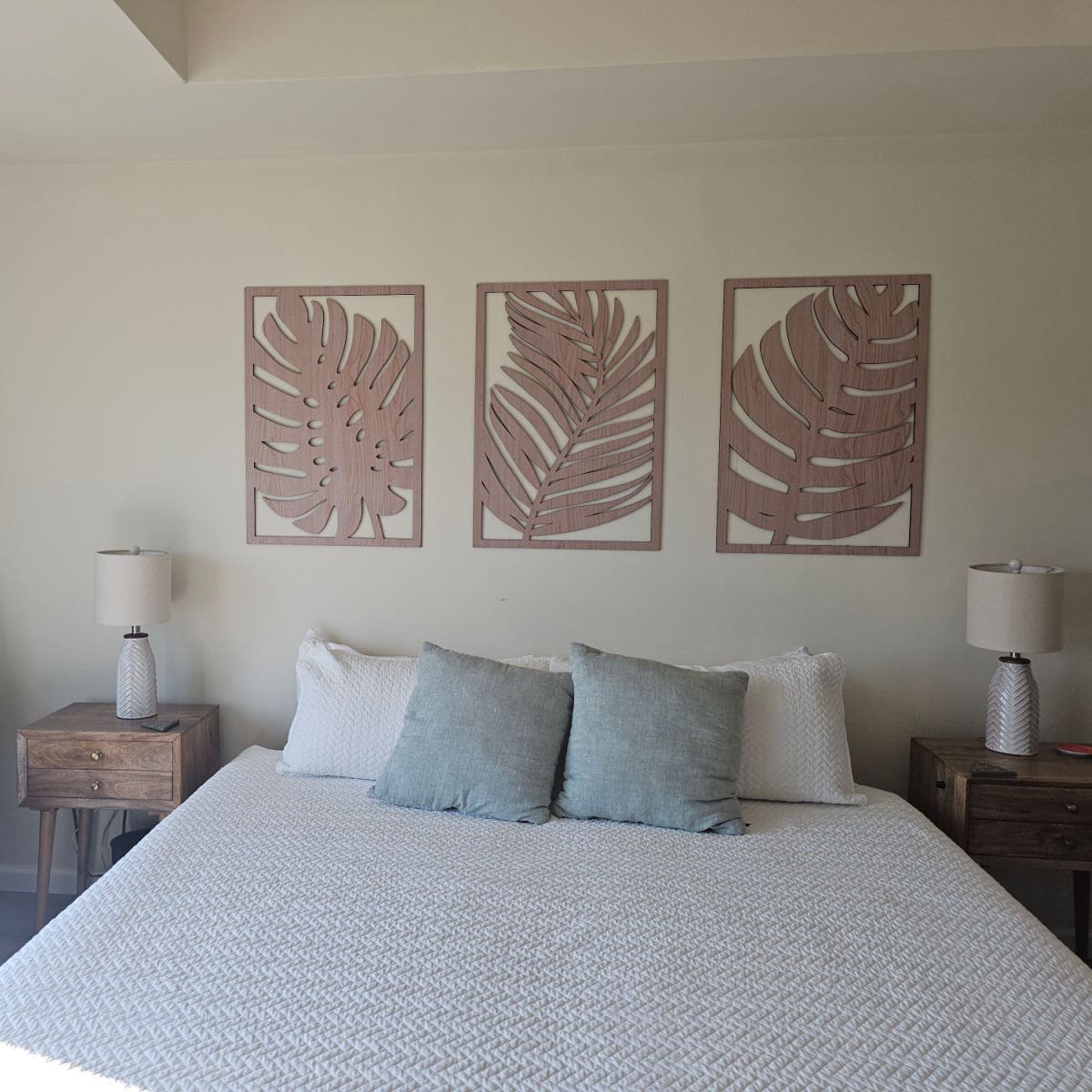 Bedroom with palm tree art on the wall, white cover on the bed with two nightstands with lamps