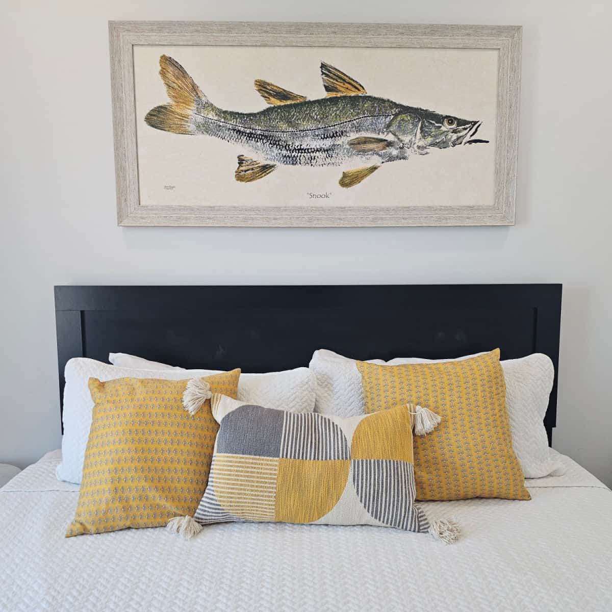 bed with white linens, yellow pillows, and a dark headboard, fish print over the bed