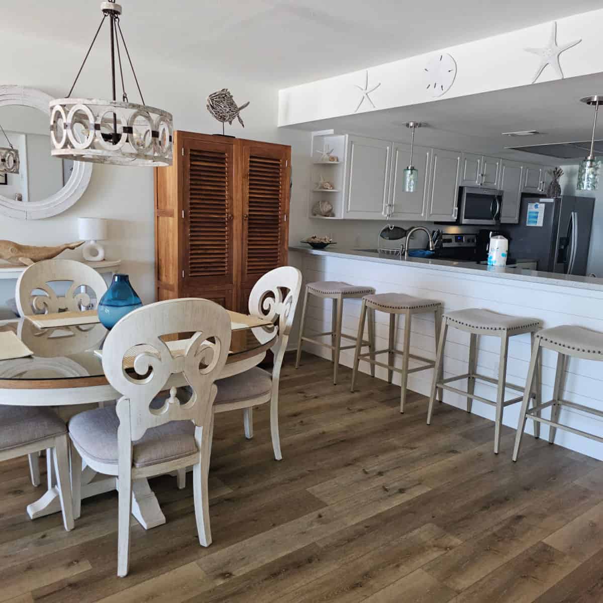 kitchen and dining room area with white chairs and stools, sand dollars and starfish art on the wall