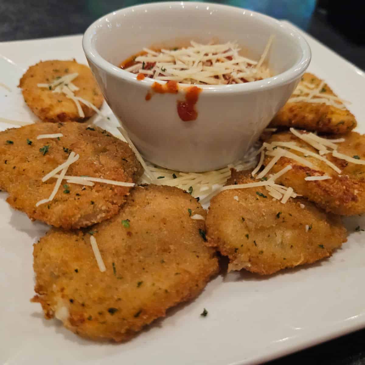 Fried mozzarella on a white plate with a white bowl filled with marina topped with fresh parmesan