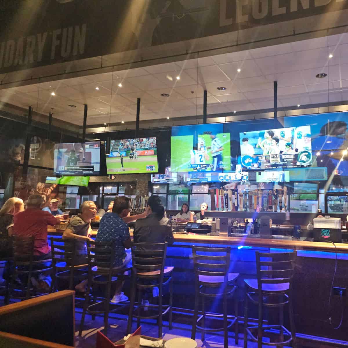 Indoor bar with tall bar stools, TV playing on 4 screens above the bar