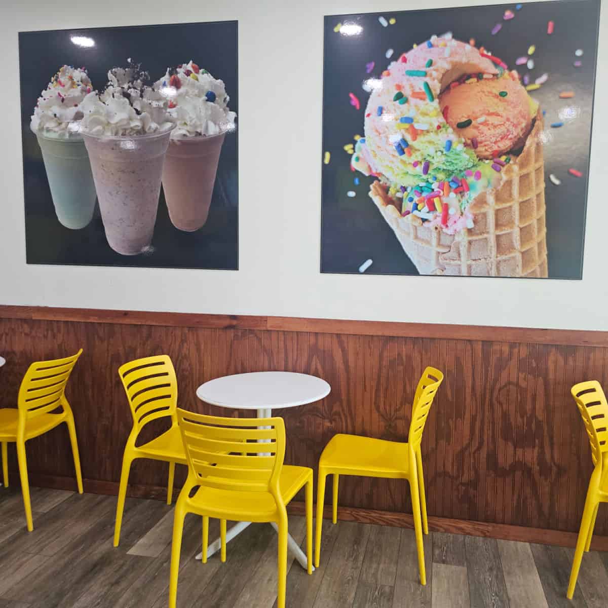 ice cream and shake photos on the wall above white tables with yellow chairs
