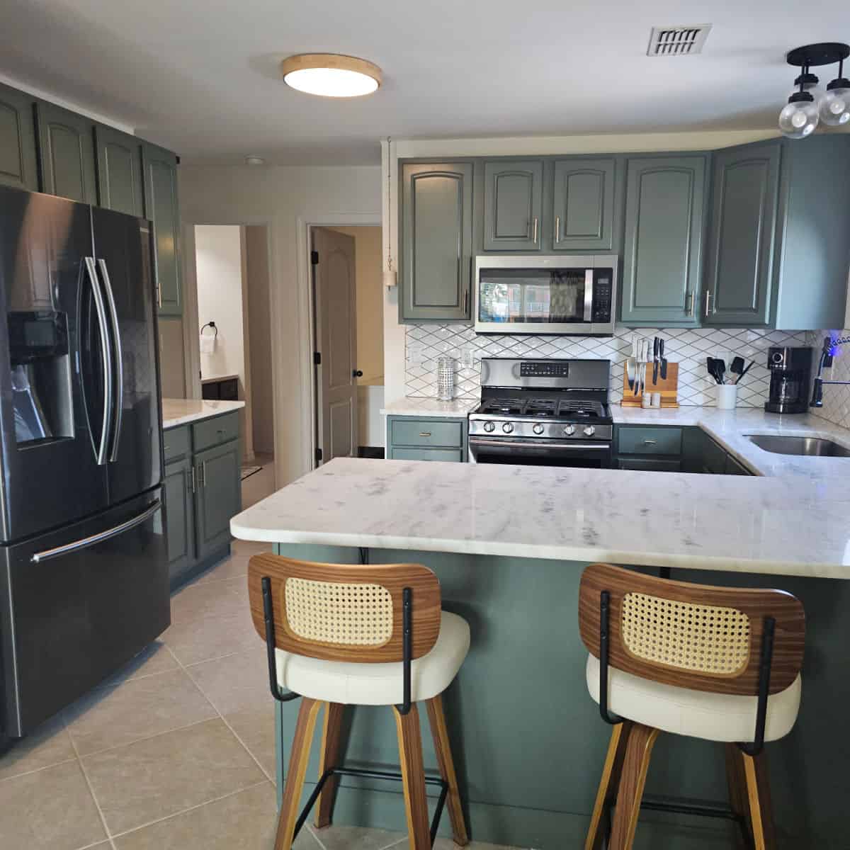 Kitchen with white counters, coastal green cabinets, and stools against the counter