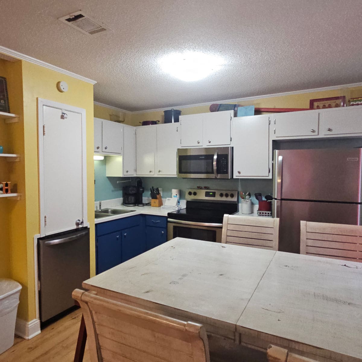 Kitchen with white and blue cabinets, art on the wall, stainless steel appliances, and dining room table