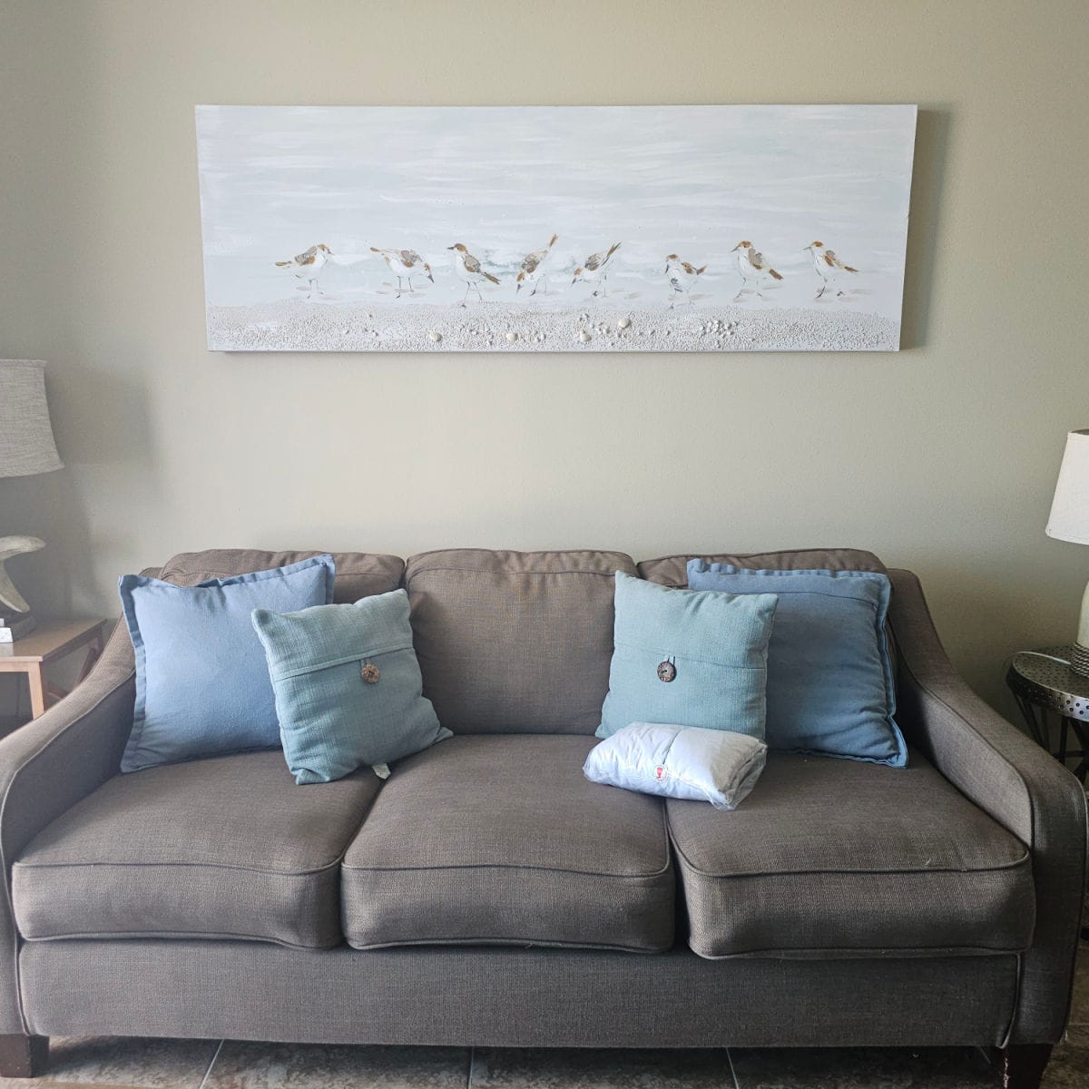 living room with a brown couch and blue pillows, shorebird art over the couch