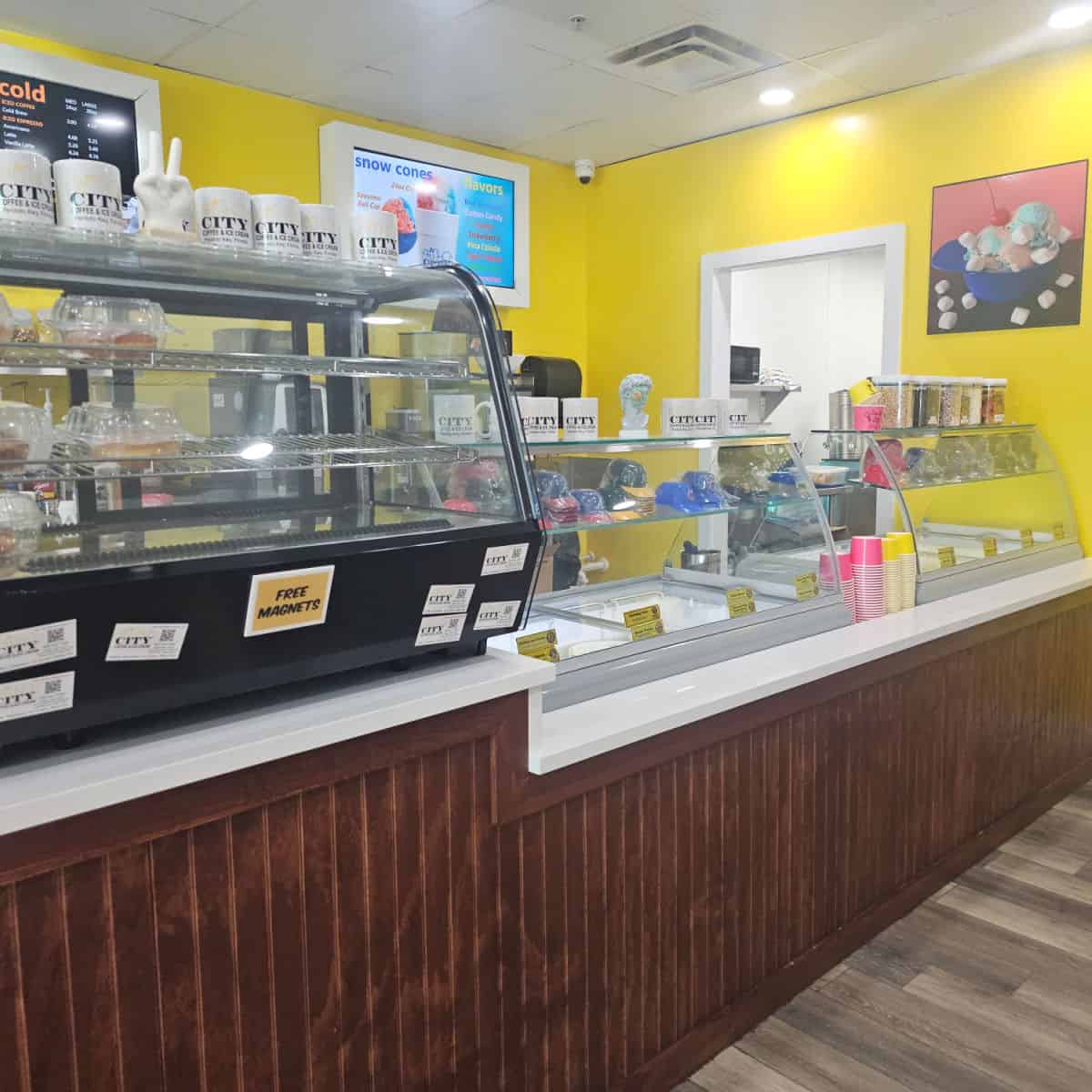 pastry display next to an ice cream counter with City Coffee & Ice Cream mugs on top, yellow walls with ice cream photo