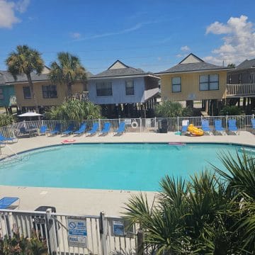 outdoor pool surrounded by colorful lifted houses, pool chairs around the pool deck.
