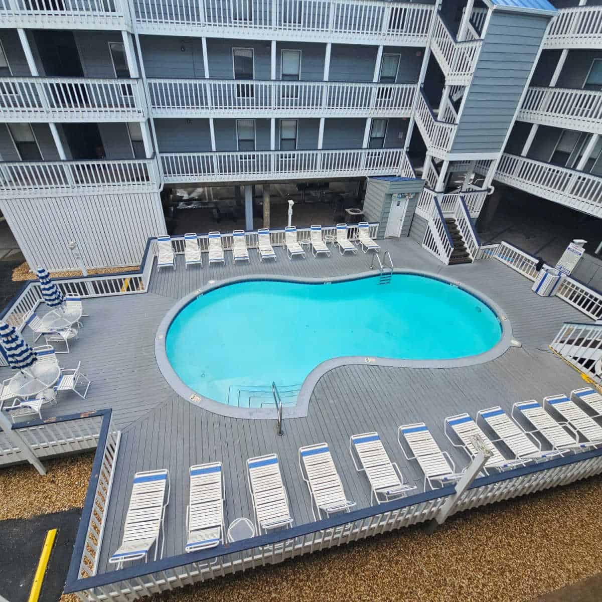 outdoor pool with buildings surrounding it, deck chairs and a couple of tables around the pool deck.