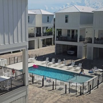 Two story Pelican Place cottages with parking underneath around the outdoor fenced in pool with lounge chairs areound the pool