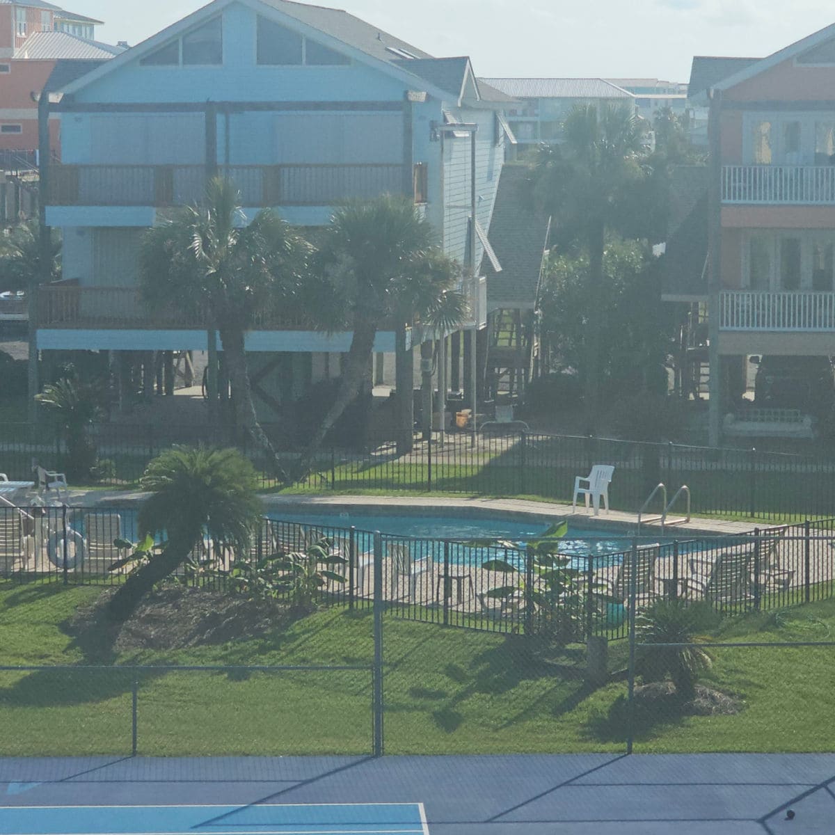 looking over the edge of a tennis court to an outdoor pool with colorful houses around in