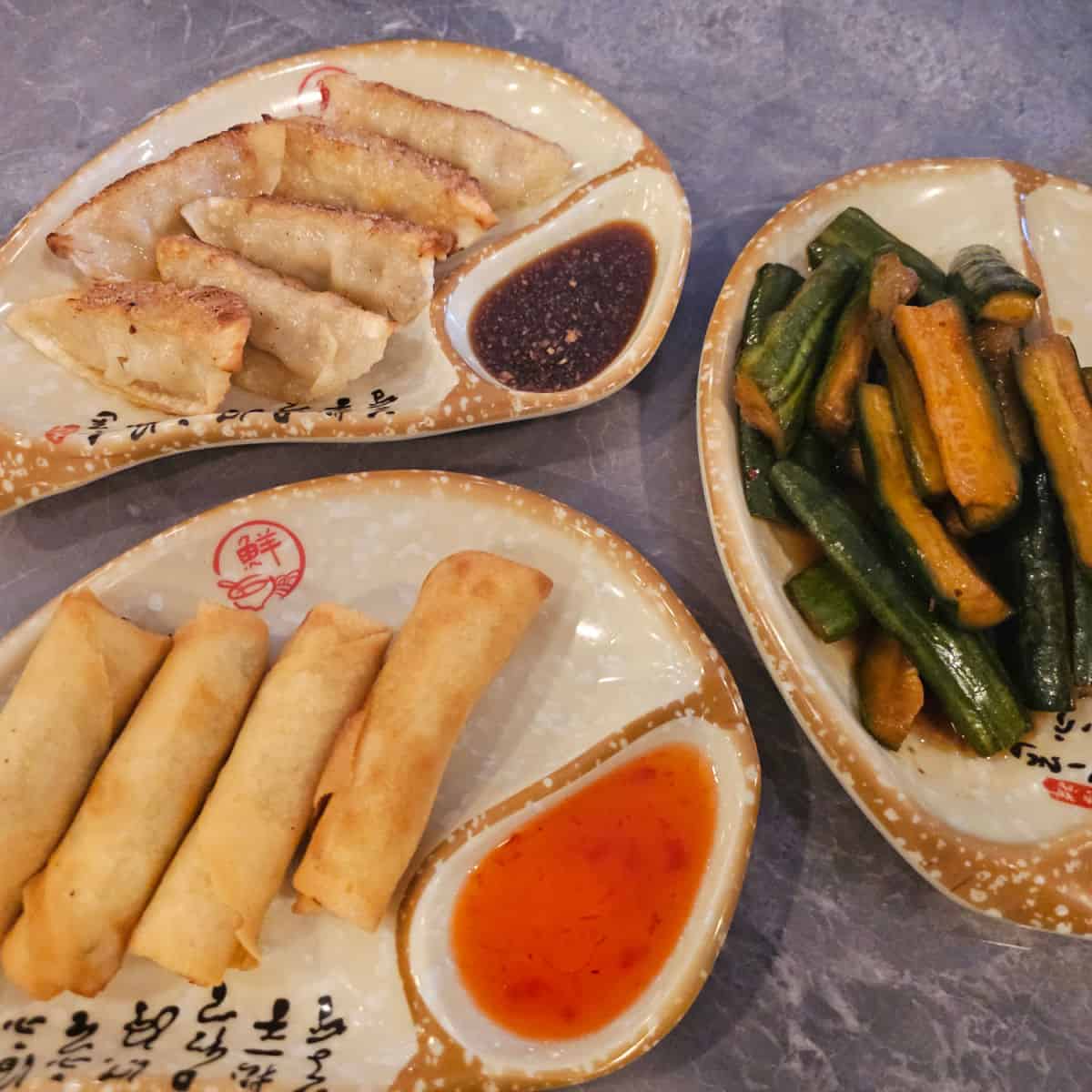 three appetizer plates with spring rolls, cucumber salad, and dumplings