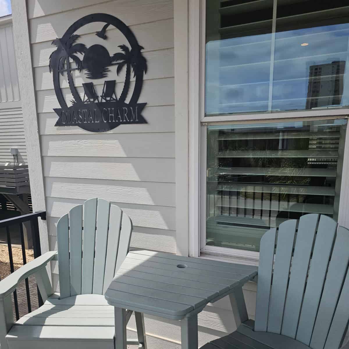 Coastal Charm sign on the side the cottage above two blue adirondack chairs by the window of the deck