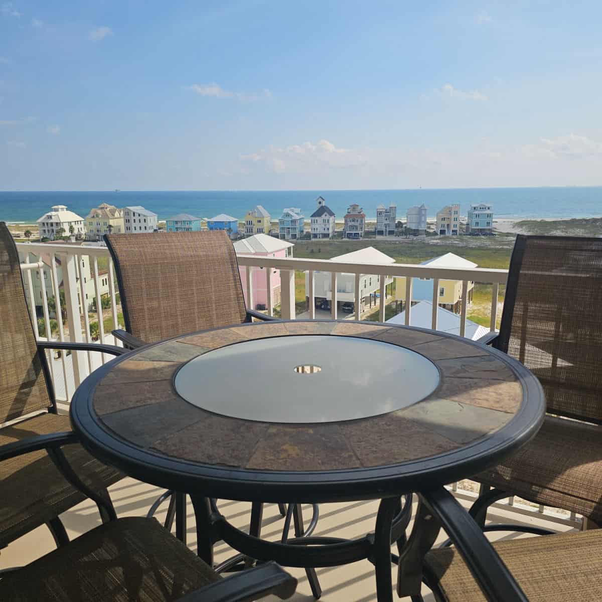 looking over tables and chairs on a balcony to beach houses and the Gulf