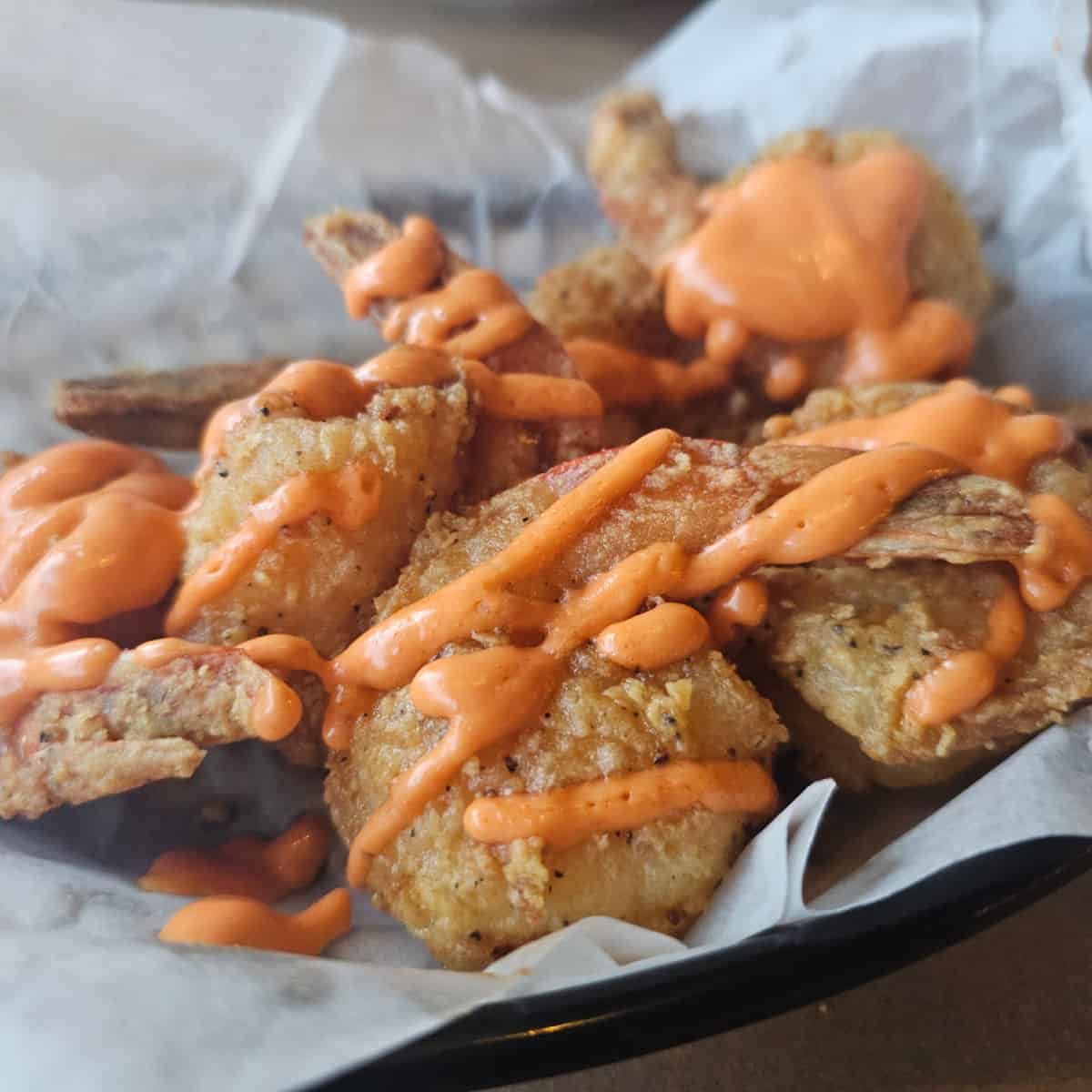 Bang Bang Shrimp in a basket with sauce drizzled over the shrimp