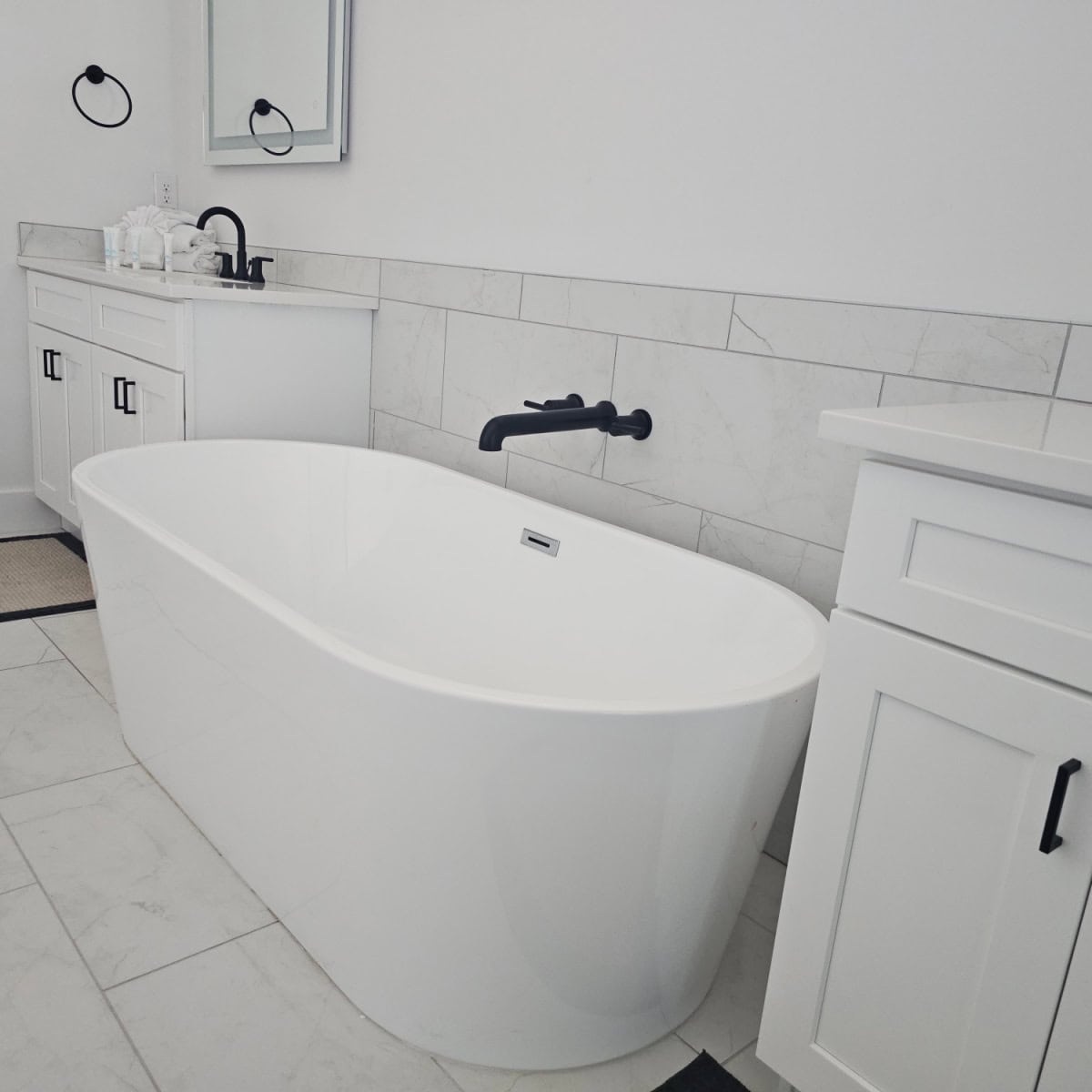 Large white bathtub with a faucet coming out of the wall, white cabinets on either side of the bathtub