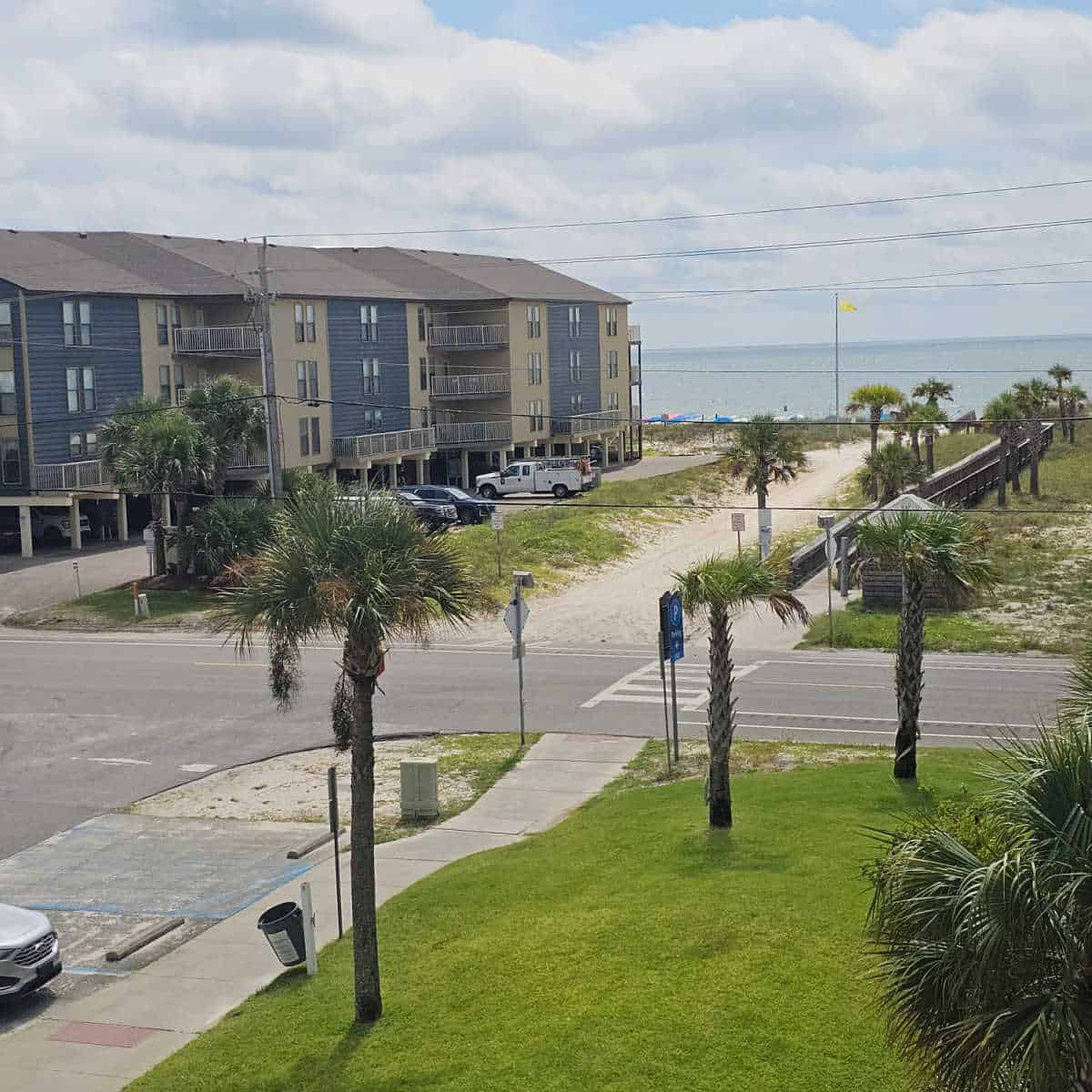 looking across grass and palm trees to West Beach Blvd then the 10th street beach access with a boardwalk towards the beach