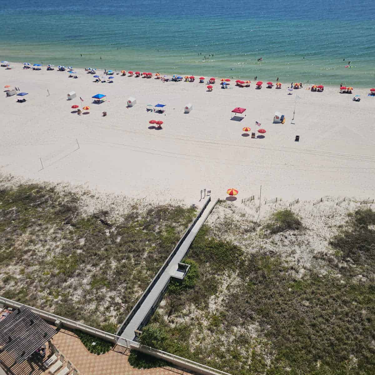 looking down to the beach with a wooden boardwalk over the sand dunes, beach umbrellas spread out near the water