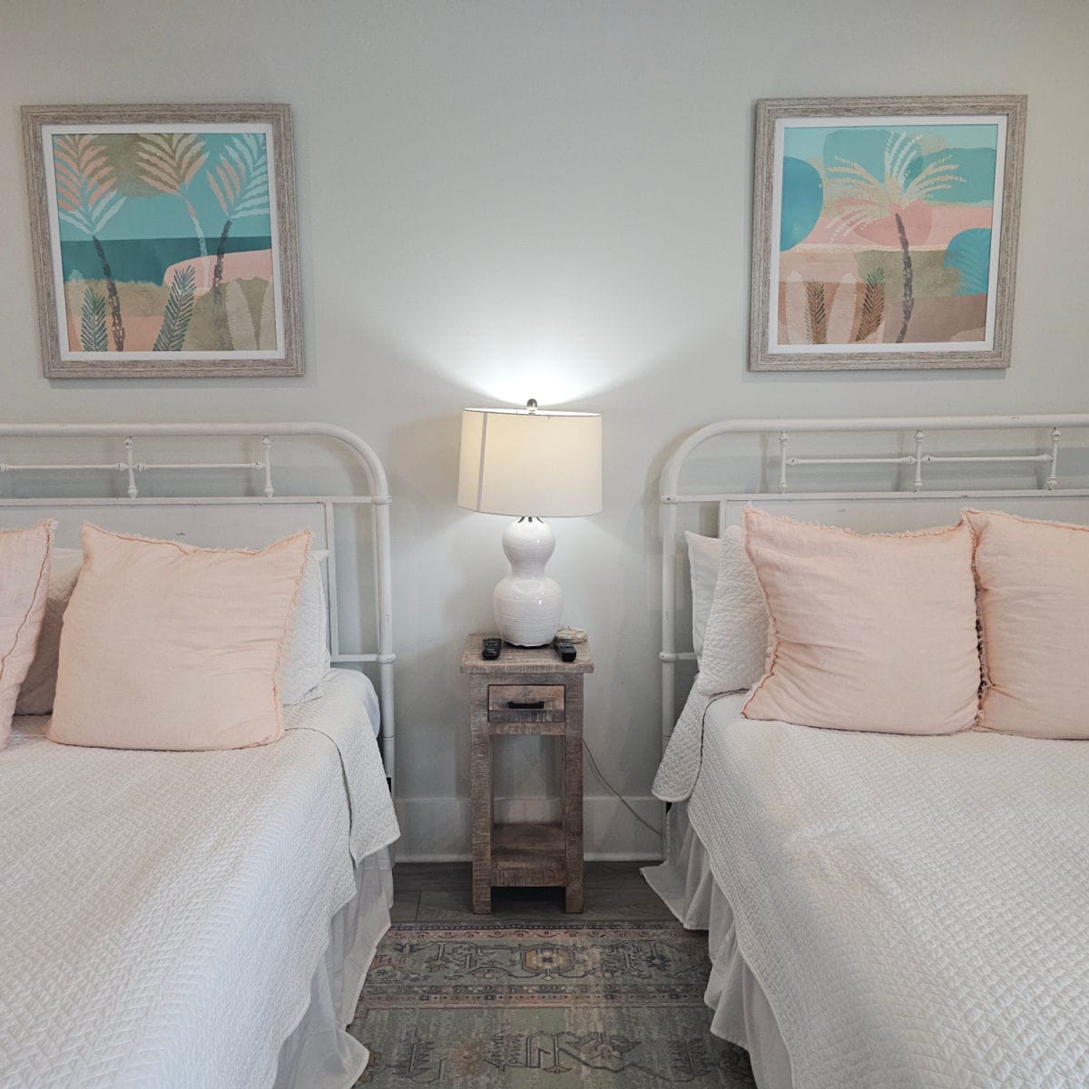 two beds with white linens and pink pillows small nightstand between the beds, two art prints above the beds