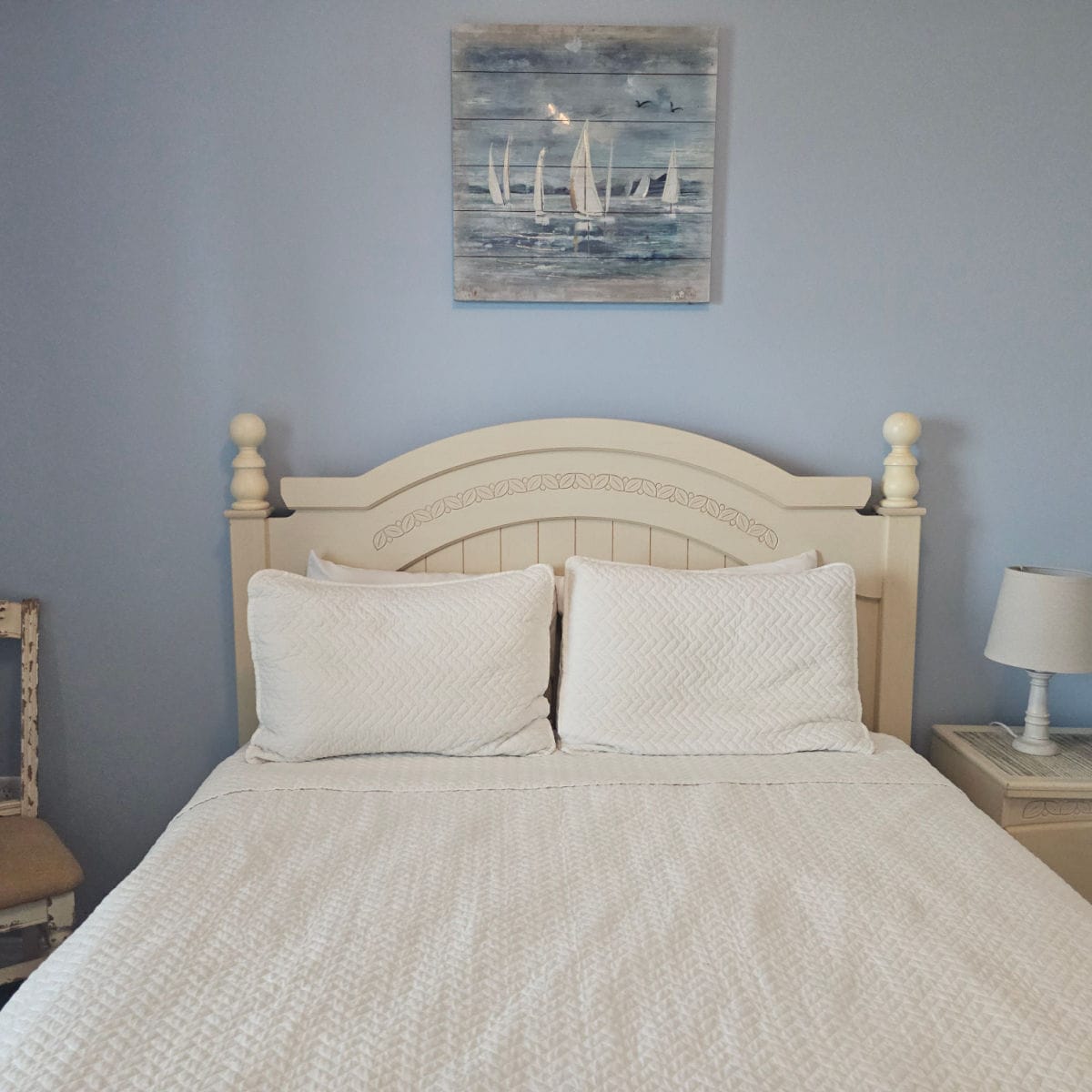 bedroom with blue walls, bed with white linens, nightstand with a white lamp