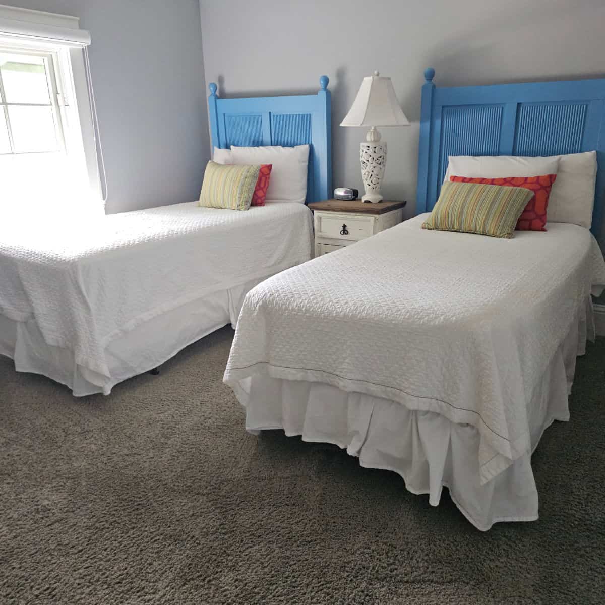 Bedroo with two twin beds, blue headboards, white linens, colorful pillows on the bed