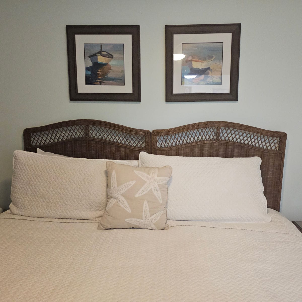 Bedroom with two boat pictures above the wooden headboard of the bed with white linens and a sea star pillow