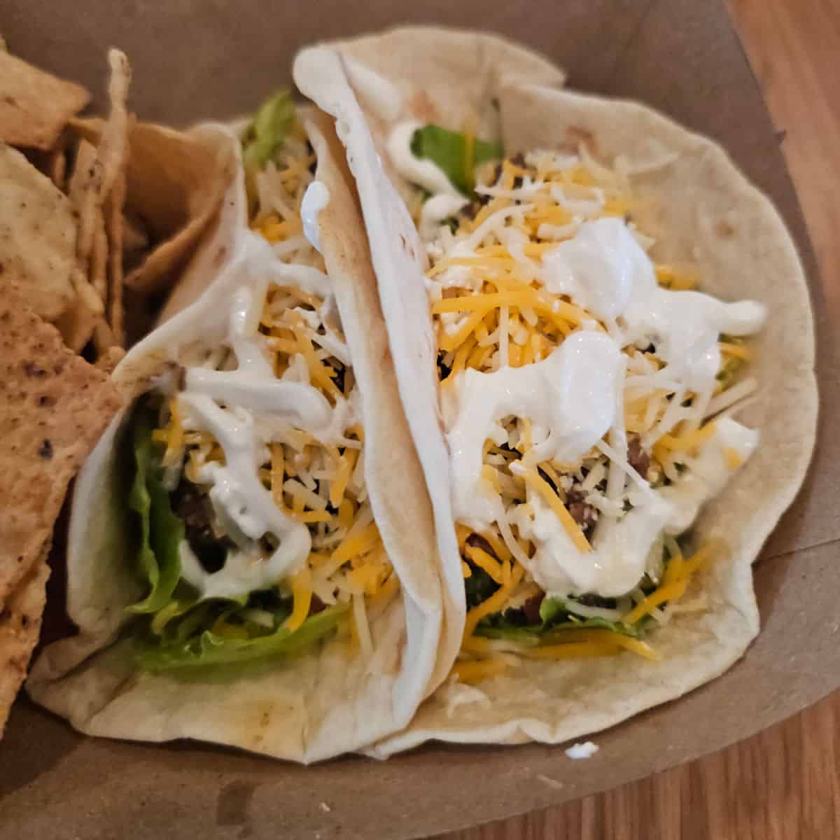 Two flour tacos in a cardboard container with chips