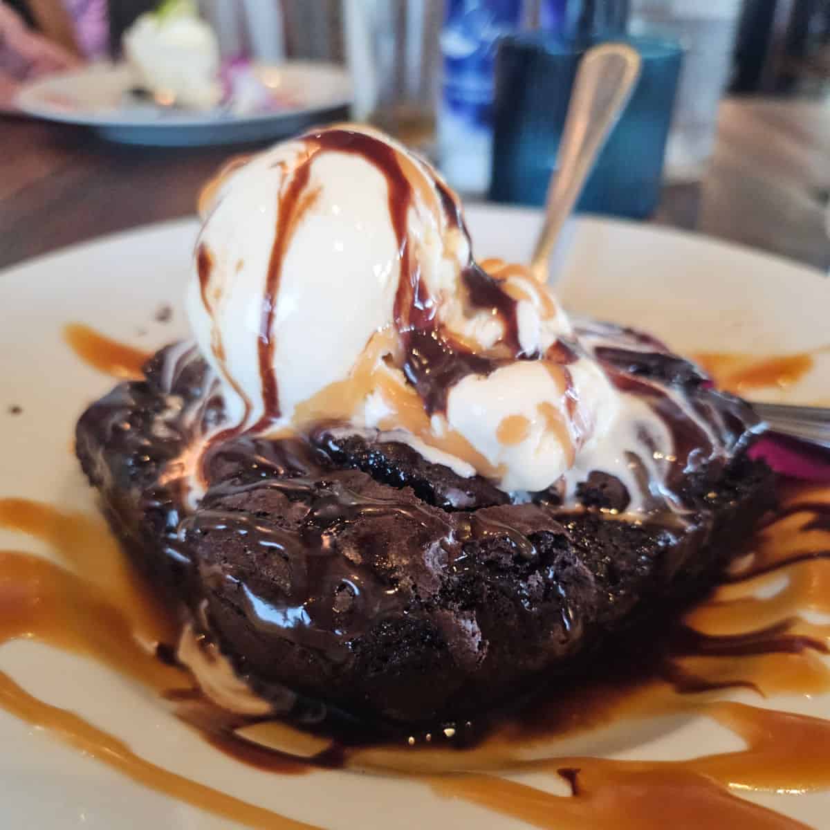 caramel and chocolate covered ice cream on top of a brownie on a white plate