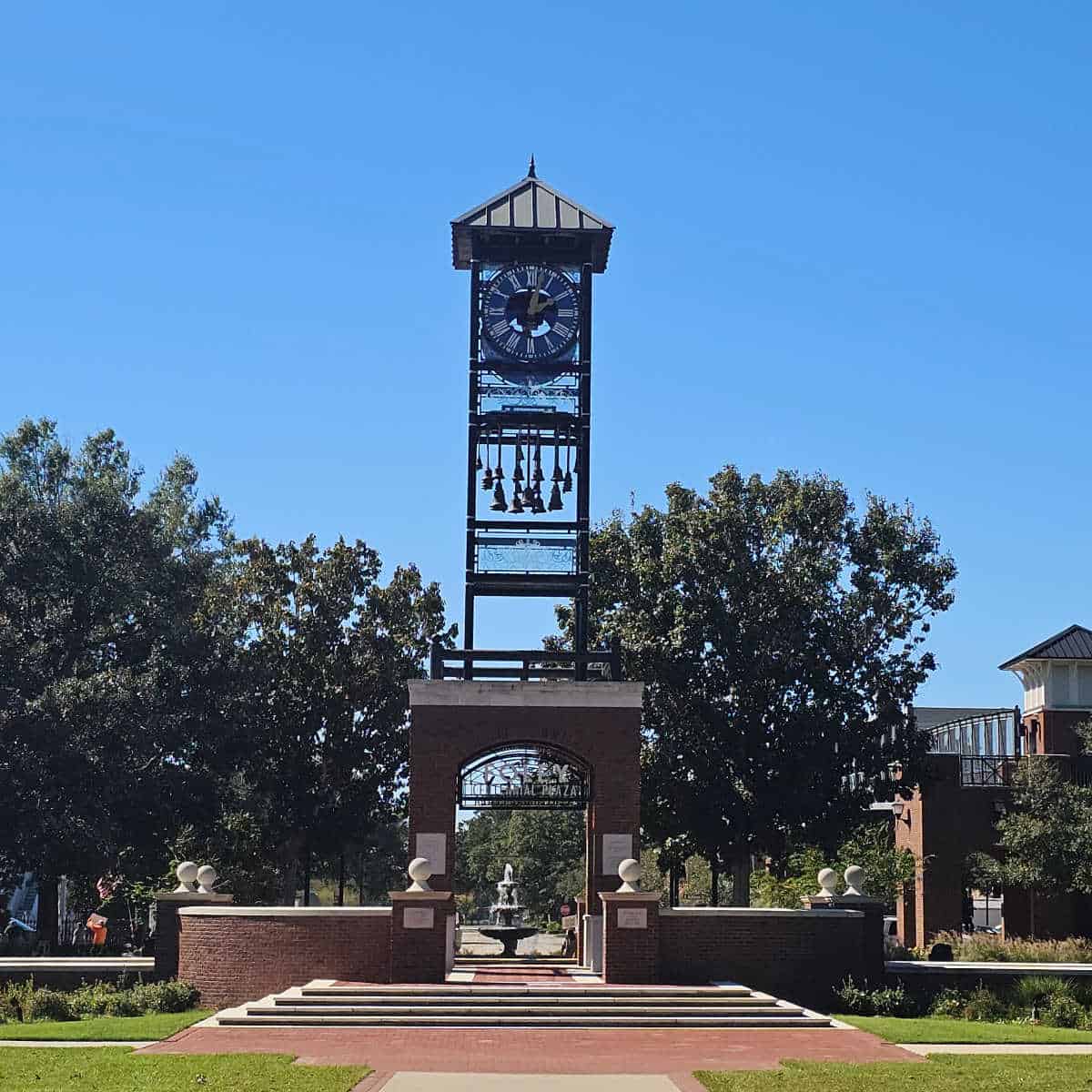 centennial plaza sign at the base of a clock tower with trees on either side
