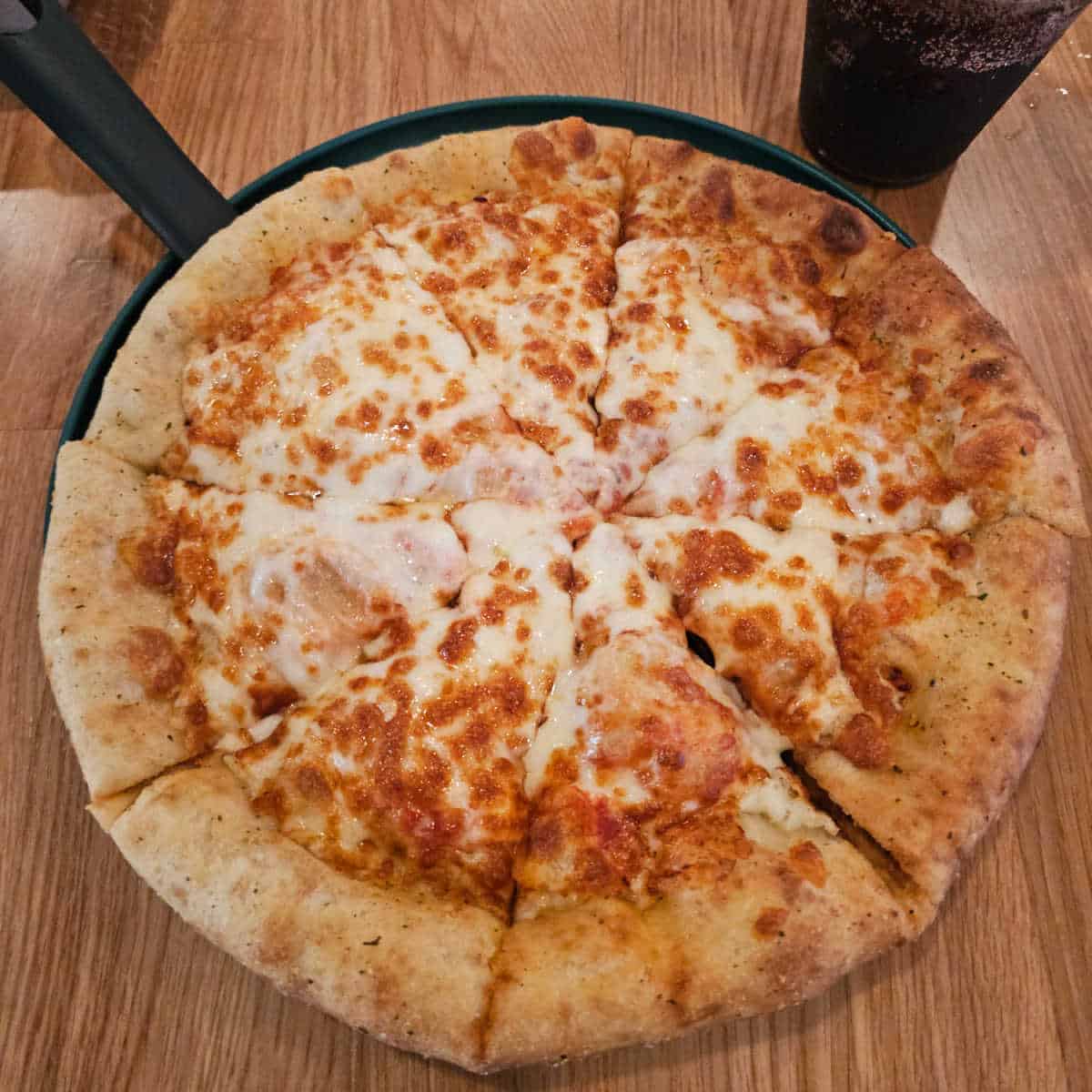 cheese pizza on a dark plate with a soda next to it